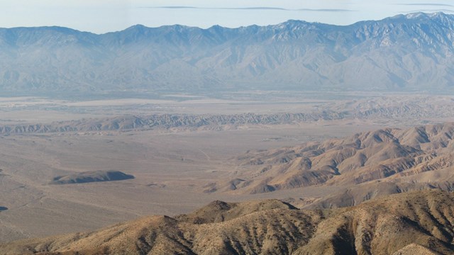 A line of small hill-like ridges in a valley, mountains in the background.