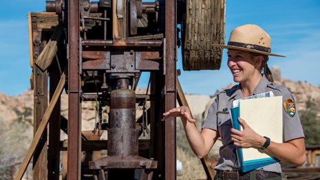 Color photo of a ranger standing in front of a historic mill structure.