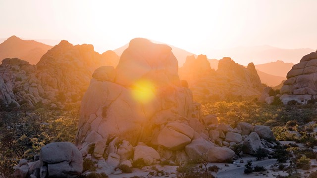 Large granite boulder piles backlit by a setting sun.