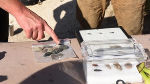Color photo of hand pointing to stone tools.