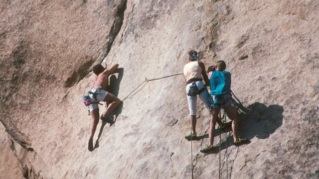 Three people rock climbing on a cliff face