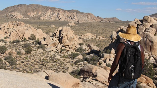 a hiker standing high on a rock outcrop looks over a desert valley