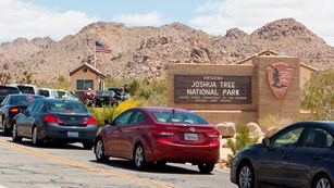 A line of cars on a road passing a sign that reads Entering Joshua Tree National Park