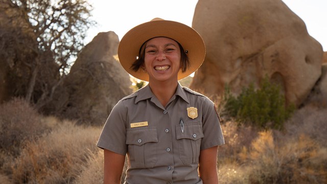 A ranger on a trail smiles widely. 