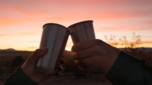 Two metal cups touching; sunset in the background. 