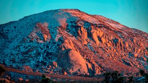 Alt text: Snow dusts the top of a mountain cast in golden light.