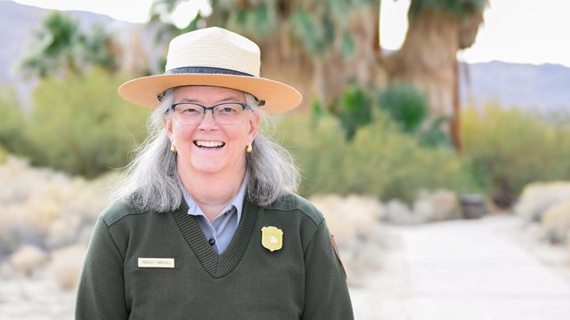 A ranger stands in front of palm trees and smiles at the camera