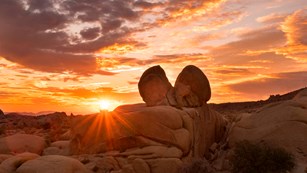 A rock shaped like a heart with a brightly colored sunrise in the background. 