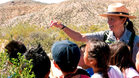 A ranger and kids surrounded by desert vegetation. 