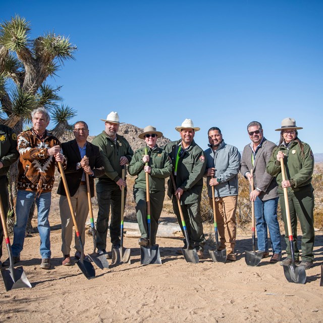 Group of people with shovels and desert backdrop.
