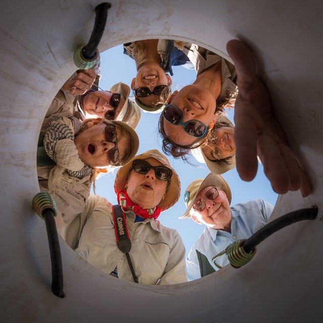 A group of people look down at camera in a hole.