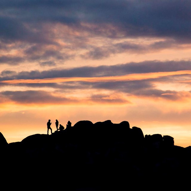 A silhouette of people on rocks under a sunset
