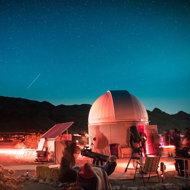 People moving around at night near observatory causing red light streaks and blue sky.