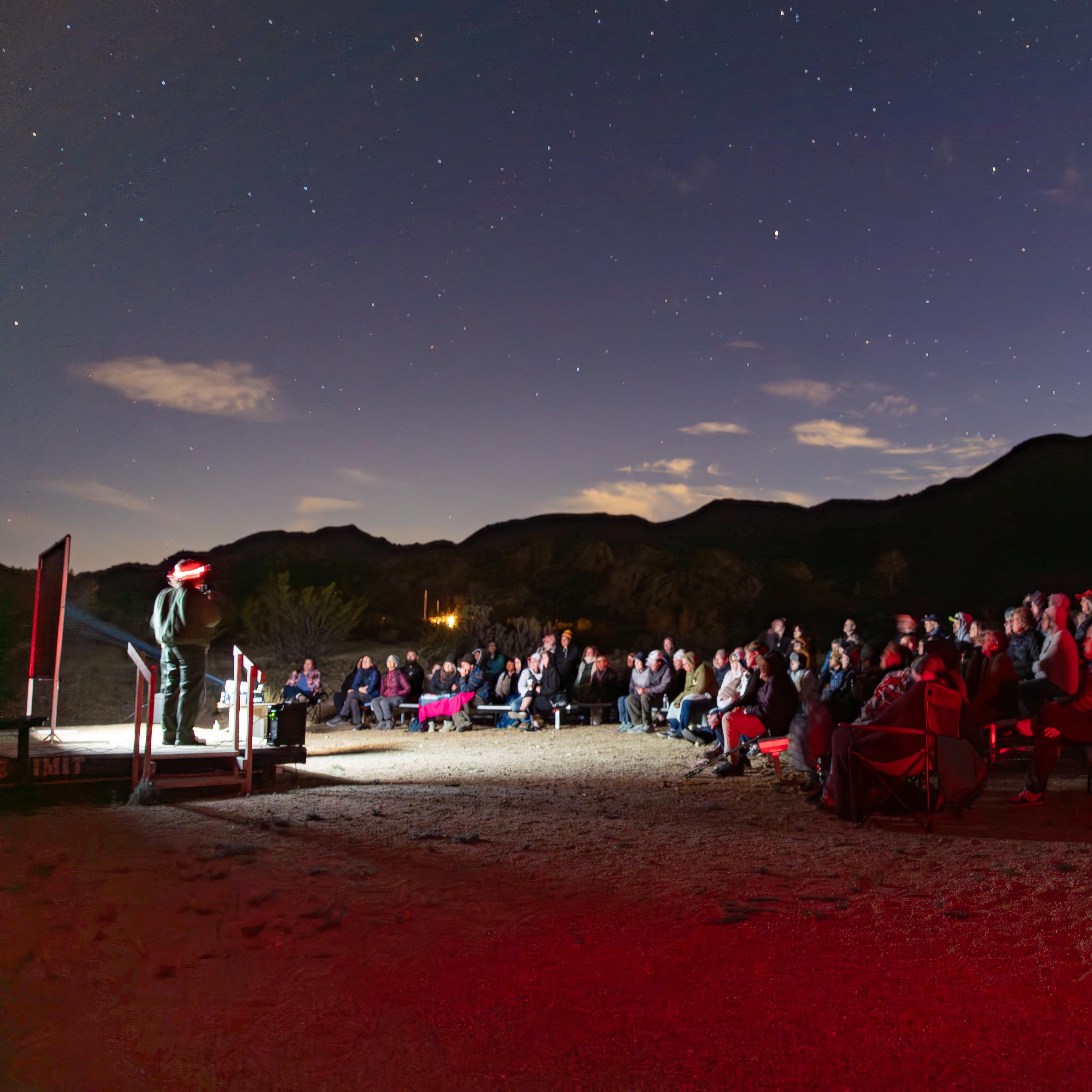 Rangers with red lights talk in front of a large audience, with the stars behind