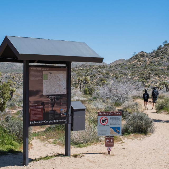 A backcountry trailhead sign labeled Black Rock Canyon with hikers to the right on a trail