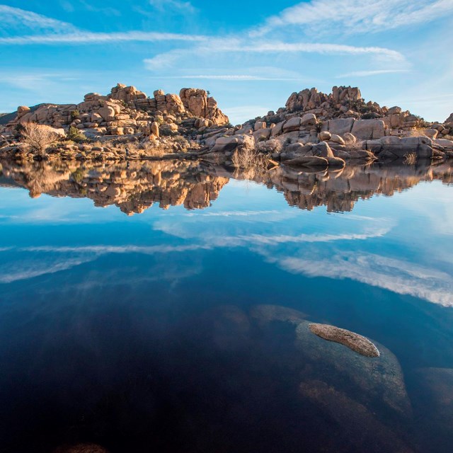 Color photo of a span of water with granite boulder piles in the distance.