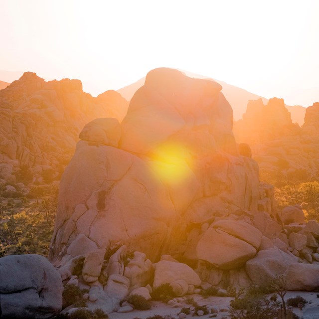 Large granite boulder piles backlit by a setting sun.