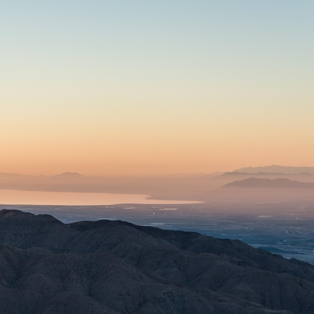 Color photo of sunrise as seen from Keys View looking out over the Salton Sea. It is very hazy/pink.