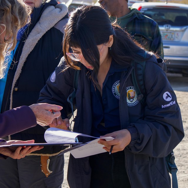 A group of people standing in a desert landscape. Two people are looking at a clipboard