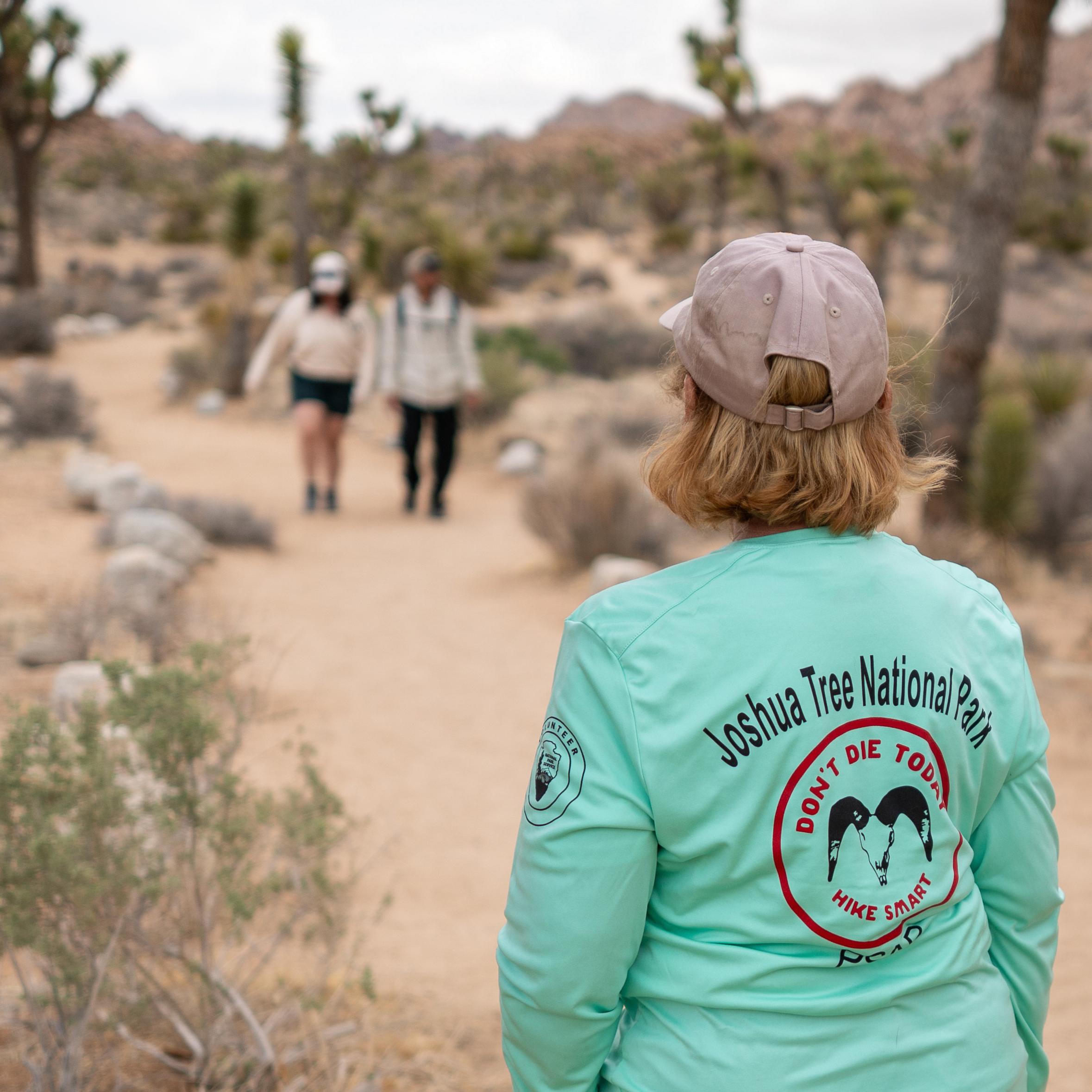 A person in a teal shirt looking down trail towards hikers