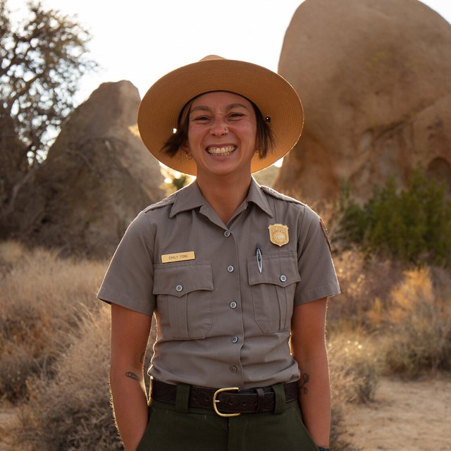 A ranger on a trail smiles widely. 