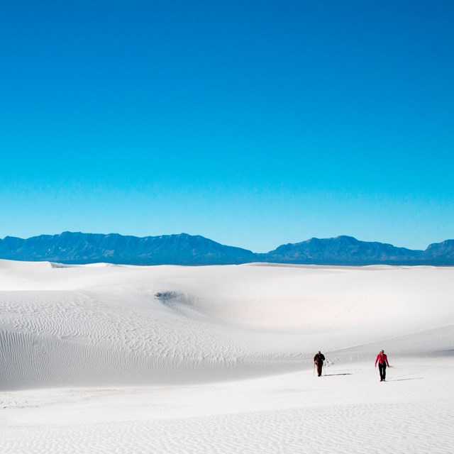 Two people walking across white sand dunes