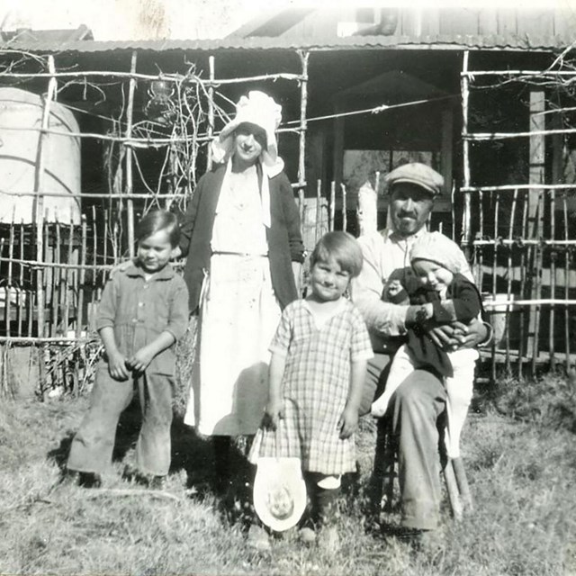 a black and white photo of a family in front of a primitive dwelling