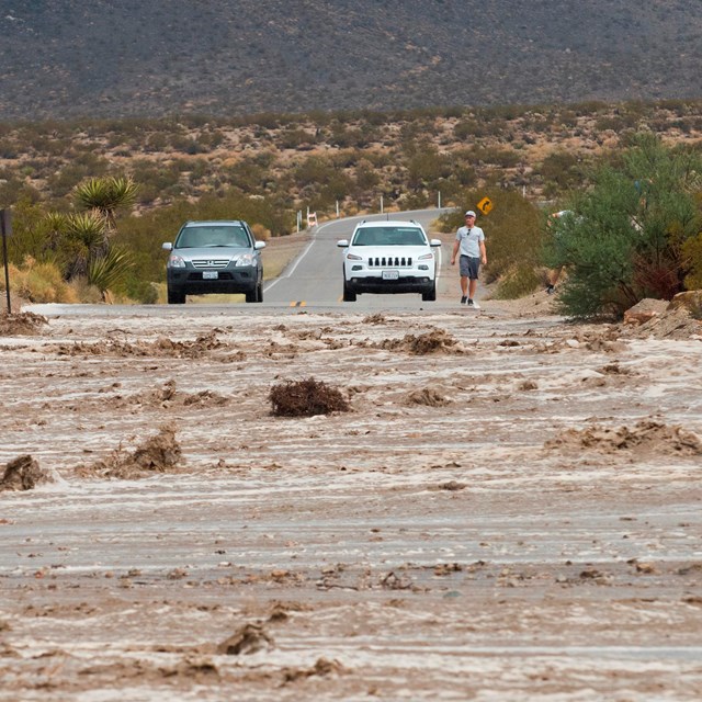 a flooded road with a car stopped before the rushing water. 