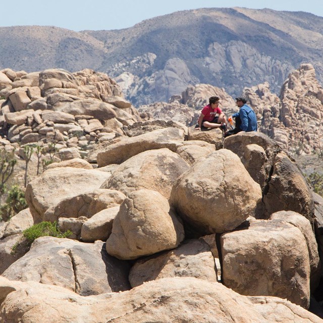two people sitting atop a rock outcrop with a mountain in the distance