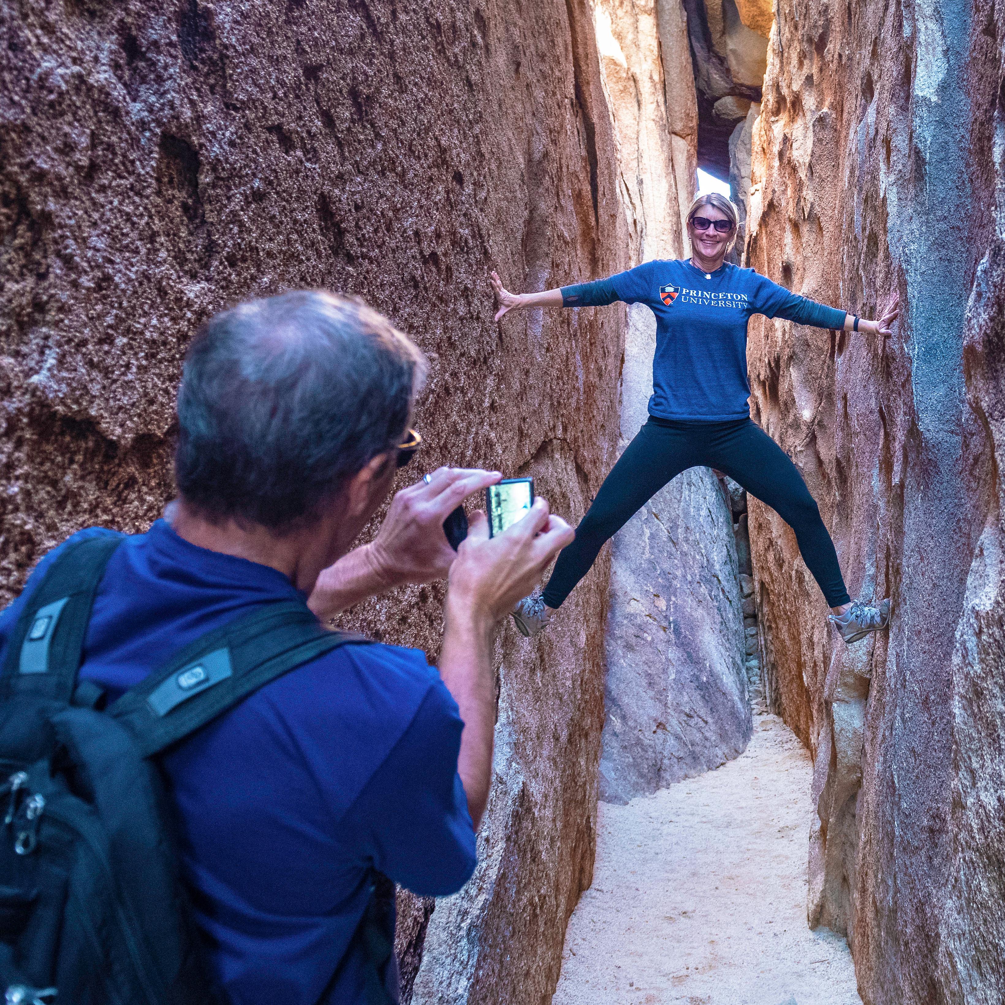 A woman poses for a photo and braces against the sides of a slot canyon.