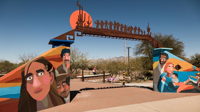 An entryway to a park with a brightly colored mural and metalwork