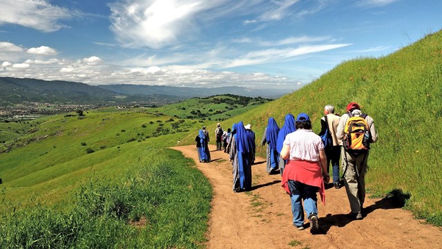 Visitors in period costumes hike along a scenic trail. 