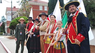 A park ranger and people in colorful costume hold flags at the Presidio of San Francisco