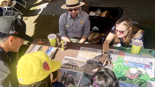 NPS employees pointing out educational materials to kids at a table