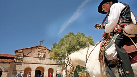 A rider sits mounted on a horse outside Mission San Antonio 