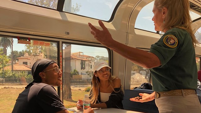 A docent talks to two young people on a train
