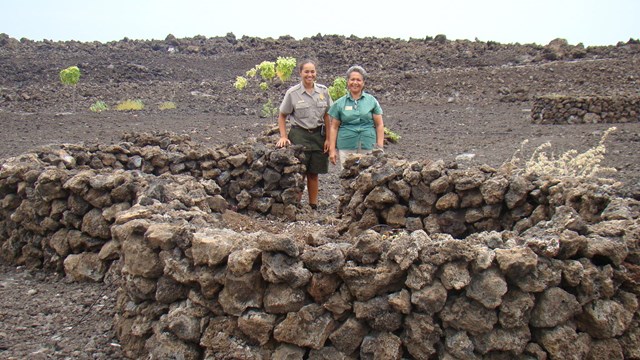 Two park employees standing next to a large planter made of lava rock