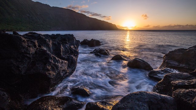 Sunset over the ocean and tall pali, cliffs. 