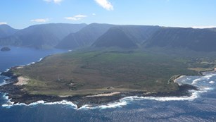 An aerial view of a peninsula with ocean on the right side and cliffs behind the peninsula..