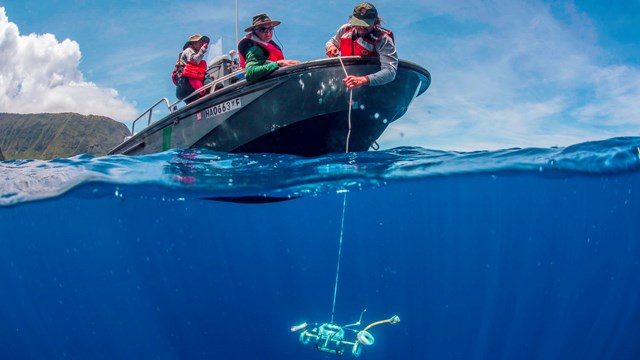 Three people on a boat and scientific equipment underwater. 