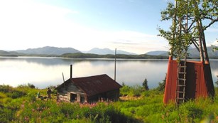 A cabin by a sunny lake, with an old windmill.