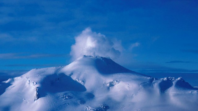Snow covered volcano peak steaming.