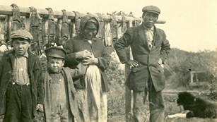 Historic family of four stands in front of a salmon drying rack.