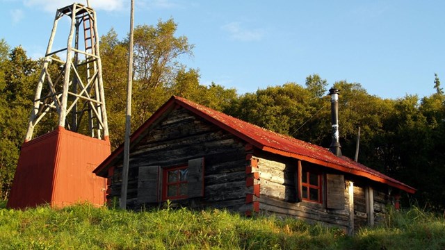 a cabin and old windmill sit on a grassy hill