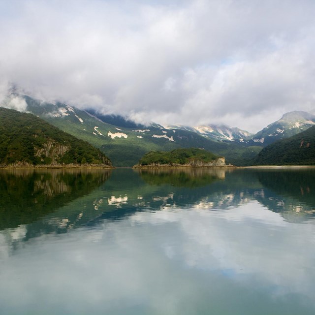 steep mountains rise abruptly from the glassy waters of a bay