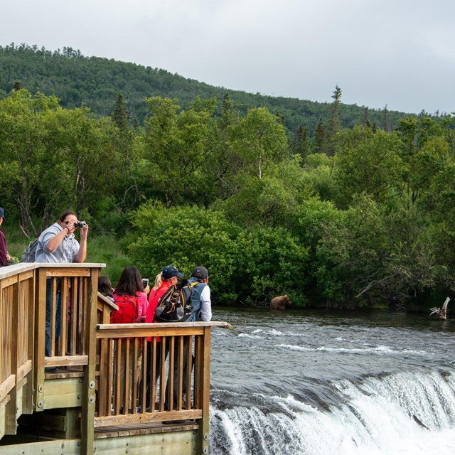 a platform in front of a waterfall with people on the platform taking photos