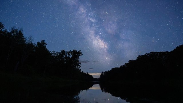The Milky Way illuminates the dark sky with millions of stars above a river.
