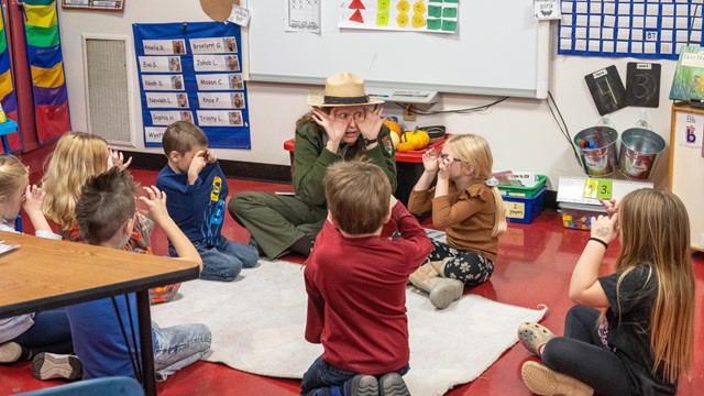 A ranger holds both hands with wide circles around her eyes as she teaches a class about owls.