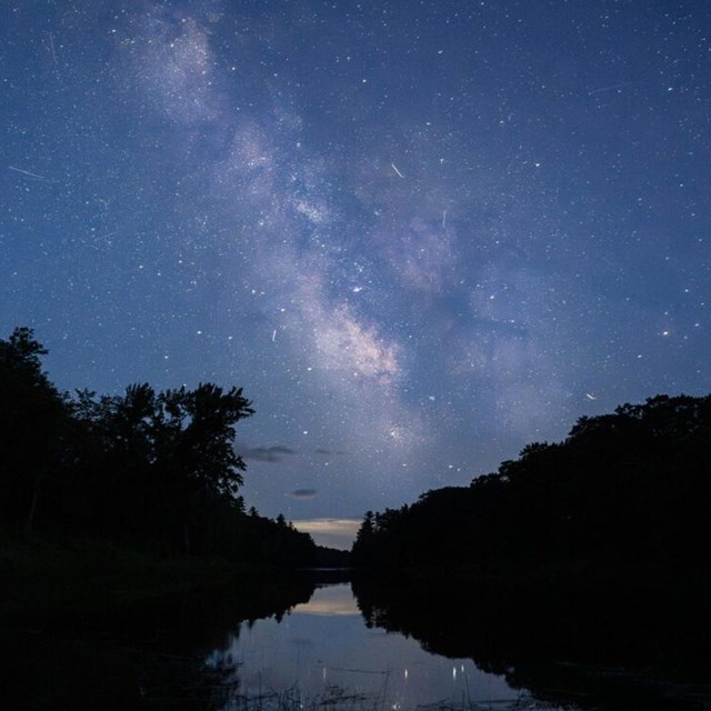 The Milky Way illuminates the dark sky with millions of stars above a river.