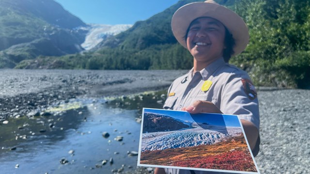 A ranger holds out a postcard with glacier behind